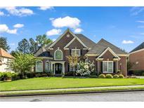 Beautiful two-story brick home with manicured lawn and lush landscaping on a sunny day at 3855 Greenside Ct, Dacula, GA 30019