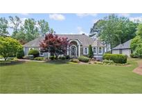 Charming home featuring a large front lawn with mature landscaping, trees, and architectural roofline at 6725 Polo Dr, Cumming, GA 30040