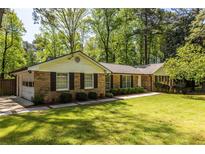 Charming brick home with attached garage and well-manicured front lawn and mature trees at 1602 Shamrock Se Trl, Smyrna, GA 30080