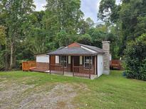 Charming cottage-style home with a brick facade, covered porch, and wooden deck nestled amongst lush greenery at 6925 Buchanan Hwy, Dallas, GA 30157