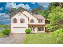 Inviting two-story home with a well-manicured lawn, attached garage, and lake view at 7737 Bar Harbor Dr, Riverdale, GA 30296