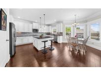 Modern kitchen features white cabinetry, stainless steel appliances, dark countertops, and an island with barstool seating at 5950 Hidden Ridge Ct, Cumming, GA 30028