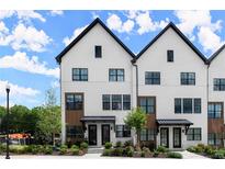 Modern townhome exterior featuring black-framed windows, a painted brick facade, and well manicured landscaping at 654 Soul Aly # 102, Alpharetta, GA 30009