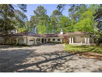 Mediterranean-style home with brick driveway, multiple garages, and covered porch, framed by mature trees at 9355 Huntcliff Trce, Sandy Springs, GA 30350