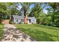 Charming blue home with a brick chimney and a spacious front yard surrounded by lush trees and a concrete driveway at 1541 Pontiac Se Pl, Atlanta, GA 30315