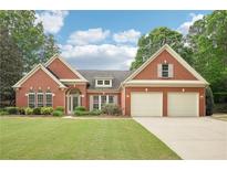 Charming brick home featuring a well-manicured lawn, mature trees, and a two-car garage at 1675 Bookhout Dr, Cumming, GA 30041