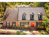 Charming brick home with an orange double-door entrance and mature landscaping, and dormer windows at 3485 Aubusson Trce, Johns Creek, GA 30022
