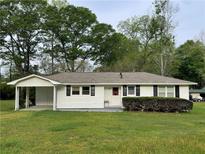 Charming single-story home with white siding, black shutters, and a covered carport nestled amongst mature trees at 66 Lakeshore Dr, Bowdon, GA 30108