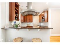 Modern kitchen featuring wooden cabinets, granite countertops, stainless steel vent hood, and two bar stools at 1125 Briarcliff Ne Pl # 14, Atlanta, GA 30306
