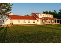 Expansive white farmhouse with a red roof, offering charm and curb appeal against a lush green lawn at 4076 Airline, Mcdonough, GA 30252