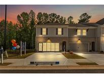 Modern townhome with brick and siding facade, two-car garage, and professionally landscaped front yard at dusk at 4667 Larkfield Way, Powder Springs, GA 30127