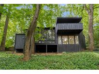 Modern home boasts dark exterior, balcony, and walls of windows amongst mature trees at 5020 Vallo Vista Ct, Atlanta, GA 30342