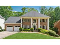 Stately brick home featuring a three-car garage and a beautifully manicured lawn with lush landscaping at 320 Rossiter Rdg, Alpharetta, GA 30022