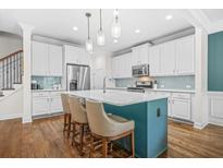 Modern kitchen features white cabinets, a teal island with seating, stainless steel appliances, and beautiful pendant lighting at 2292 W Village Junction Se Way, Smyrna, GA 30080