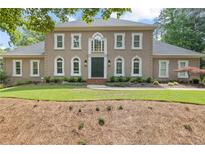 Elegant two-story home featuring a neutral facade, complemented by symmetrical windows and lush landscaping at 9950 Farmbrook Ln, Johns Creek, GA 30022