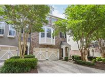 Brick townhome featuring a two-car garage and a charming covered entrance, complemented by mature trees and manicured landscaping at 6080 Indian Wood Se Cir, Mableton, GA 30126