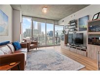 Bright living room with hardwood floors, city views, and a comfortable leather sofa and armchairs at 860 Peachtree Ne St # 904, Atlanta, GA 30308