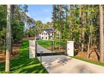 View of gated entrance and long drive to a stately, modern farmhouse nestled in a wooded lot at 400 Auburn Rd, Auburn, GA 30011
