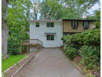 View of the home's exterior with a two-car driveway and stairs to front deck nestled in a wooded landscape at 2551 Park Se Rd, Smyrna, GA 30080