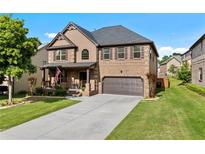 Traditional brick home featuring a covered porch, two-car garage, mature landscaping, and a well-manicured lawn at 1212 Overlook Lake Dr, Dacula, GA 30019