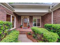 Charming brick home entrance with a wooden door, brick porch, and lush green landscaping at 9395 Clublands Dr, Alpharetta, GA 30022