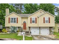 Charming yellow split-level home features brown shutters, attached two-car garage and manicured lawn at 1358 Stoneleigh Way, Stone Mountain, GA 30088