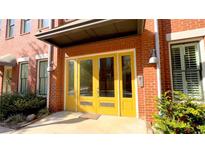 Inviting red brick townhome featuring a bright yellow front door, decorative sconces, and trimmed landscape at 4143 N Swann St, Covington, GA 30014