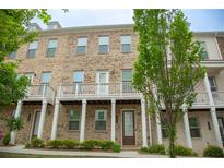 Brick townhome featuring covered front porch, white railing and front yard with green shrubs and trees at 753 Topsail Ln, Alpharetta, GA 30005