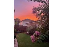 A serene backyard showcases lush green grass, a dark wood fence, blooming Crepe Myrtle, and a picturesque sunset sky at 6575 Eli Davis Rd, Cumming, GA 30040