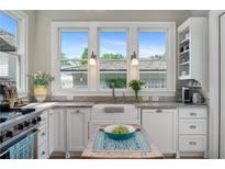 Bright kitchen featuring white cabinetry, a farmhouse sink, granite countertops, and natural light from three windows at 6575 Eli Davis Rd, Cumming, GA 30040