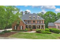 Stately brick home featuring a welcoming front porch and professionally landscaped yard with mature trees at 120 Burford Holw, Alpharetta, GA 30022