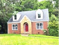 Charming red brick home featuring a stone archway, red door, dormer windows and a well-manicured lawn at 1001 Jefferson Ave, Atlanta, GA 30344