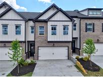 Modern townhome showcasing a two-car garage, gray brick, white siding, and black trim against a blue sky at 5706 Urban Village Way # 4, Tucker, GA 30084