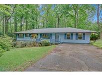 Charming single-story home featuring blue siding, a welcoming front porch, and a lush, wooded lot at 4856 Rock Haven Dr, Lilburn, GA 30047