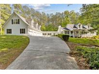 Inviting white home featuring an expansive driveway and a charming front porch surrounded by lush greenery at 1981 Luke Edwards Rd, Dacula, GA 30019