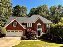 Beautiful two-story red brick home with manicured lawn, lush landscaping, and a two-car garage at 420 Windswept Ct, Roswell, GA 30075