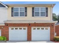 Two-story home with a double garage, brick facade, yellow siding and black shuttered windows at 988 Treymont Way, Lawrenceville, GA 30045