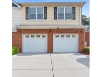 Front exterior view of a home showcasing a brick facade and a two-car garage with white doors at 988 Treymont Way, Lawrenceville, GA 30045