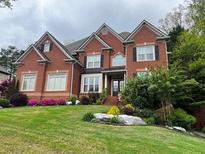 Beautiful two-story brick home with a manicured lawn, colorful flowers, and mature landscaping at 2688 Hidden Falls Ne Dr, Buford, GA 30519