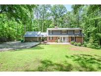 Two-story brick home with a well-manicured lawn and mature trees in a serene, wooded setting at 1216 Oleander Sw Dr, Lilburn, GA 30047
