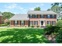 Charming two-story brick home with manicured lawn, lush landscaping, and classic black shutters at 5199 Beech Forest Sw Dr, Lilburn, GA 30047