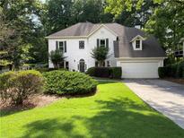 Charming white two-story home with well-manicured lawn and mature trees on a sunny day at 5440 Cameron Forest Pkwy, Johns Creek, GA 30022