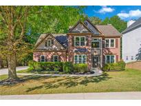Charming two-story brick home featuring a manicured lawn and mature trees creating curb appeal at 3220 Goldmist Dr, Buford, GA 30519