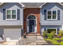 Charming home featuring a brick archway, blue door, black shutters, and a well-manicured landscaped yard at 1215 Smoke Hill Ln, Hoschton, GA 30548