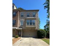 Attractive multi-story brick townhome with manicured lawn, driveway, and mature trees in the background at 288 Blue Pointe Ct, Suwanee, GA 30024