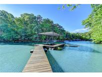 Lake view of a wooden dock with a covered sundeck in a wooded area under a bright blue sky at 975 Timber Lake Trl, Cumming, GA 30041