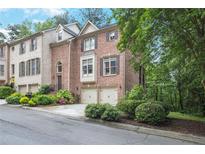 Beautiful brick townhome featuring a two-car garage and lush landscaping, enhancing its curb appeal at 7249 Village Creek Trce, Atlanta, GA 30328