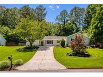 Charming single-story home with well-manicured lawn, mature trees, and inviting driveway, all under a bright blue sky at 340 Monivea Ln, Roswell, GA 30075
