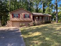 Split level home with brown siding, red shutters, and an attached garage on a wooded lot at 4865 Surrey Dr, Roswell, GA 30075
