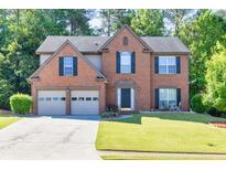 A two-story brick home with a well-manicured lawn, mature trees, and a two-car garage at 1500 Highland Farm Dr, Suwanee, GA 30024